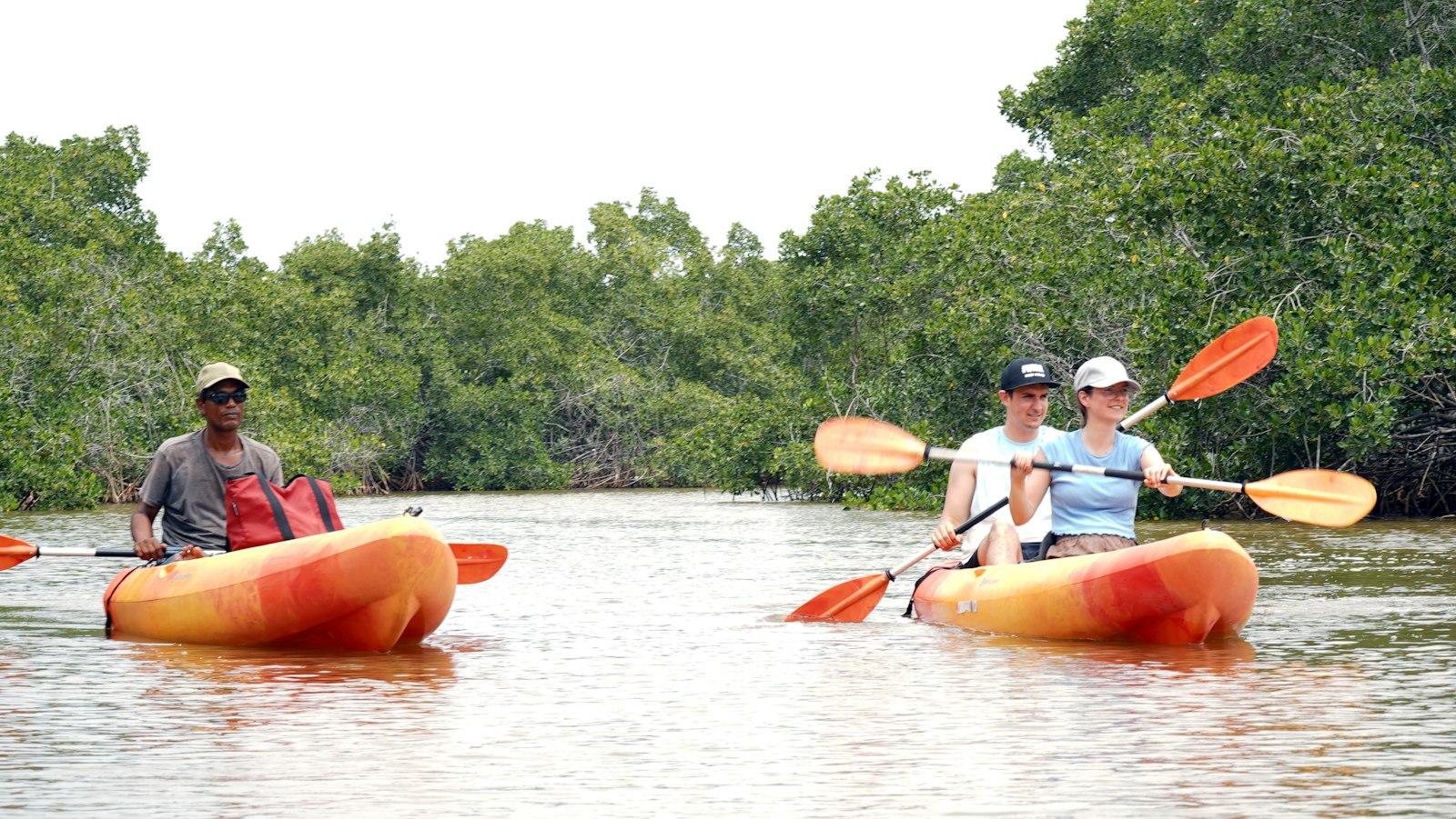 People kayaking through a calm, tree-lined waterway