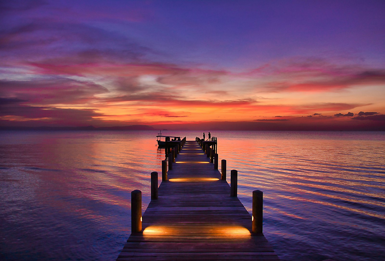 A wooden dock reaching into the sea at sunset