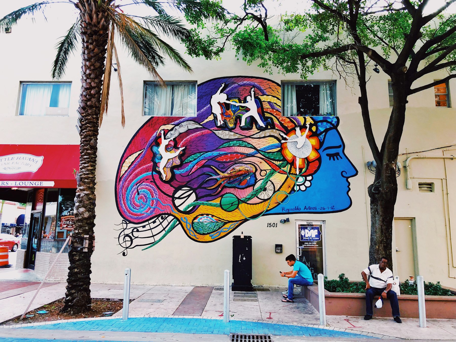 A colourful mural on a building in Little Havana with two men seated outside